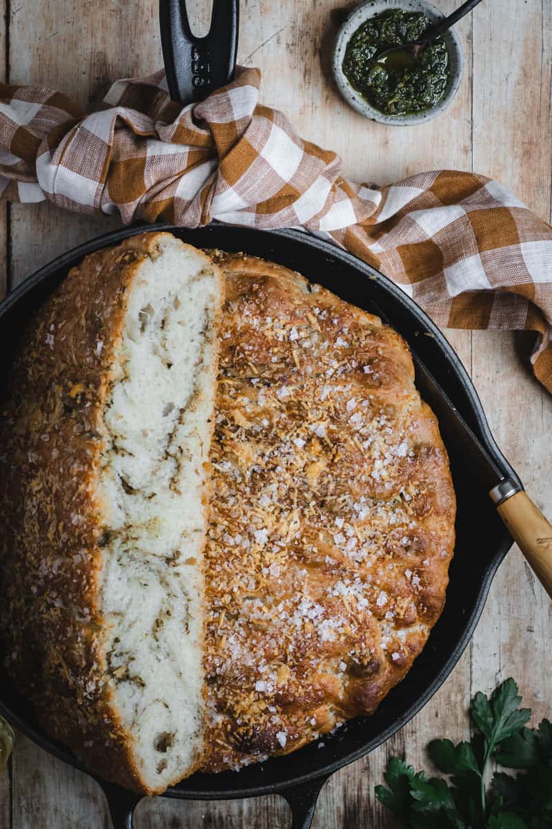 A black cast iron skillet with a pesto focaccia baked in it sits on a timber bench.