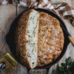 A black cast iron skillet with a pesto focaccia baked in it sits on a timber bench.