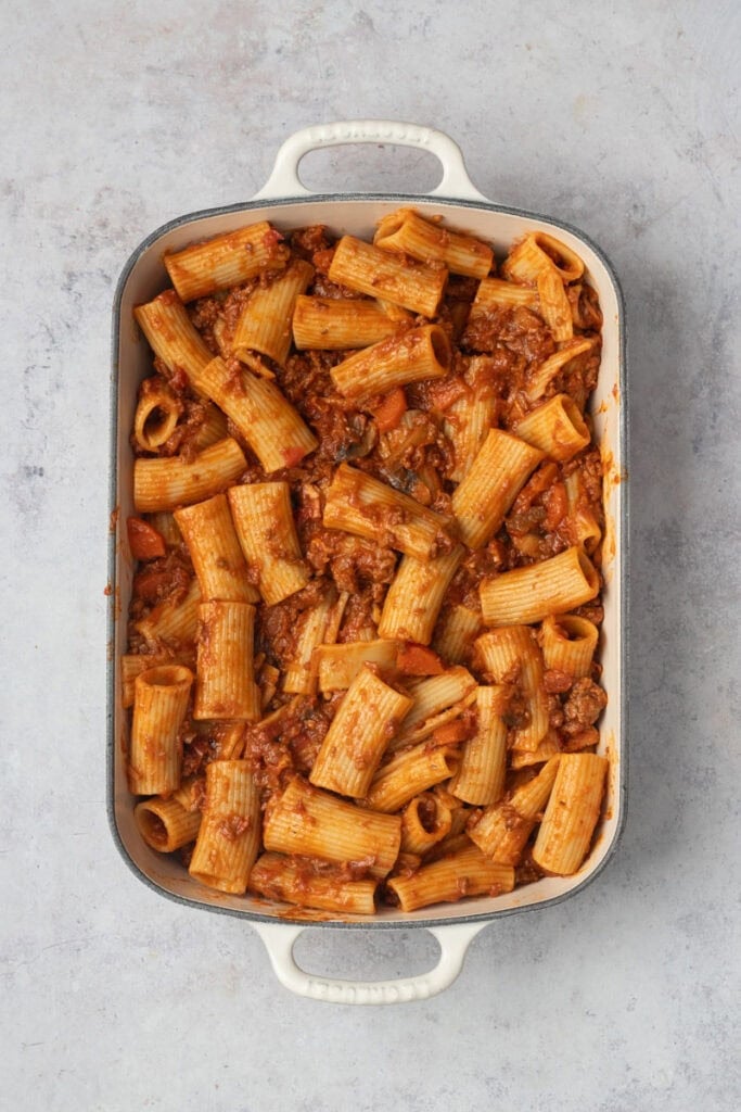 Cooked Bolognese Rigatoni in a cream colored cast iron baking dish.