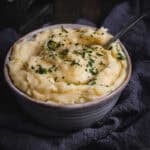 A bowl of Cheesy Mashed potatoes with parsley and salt.