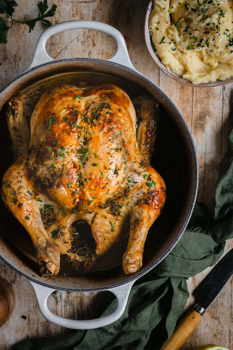 Roasted chicken in a Dutch oven with potatoes and herbs.