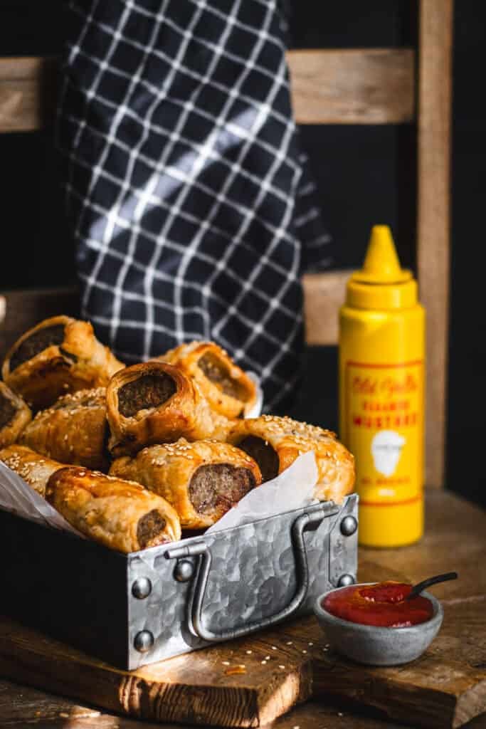 A tray of sausage rolls with ketchup and mustard.