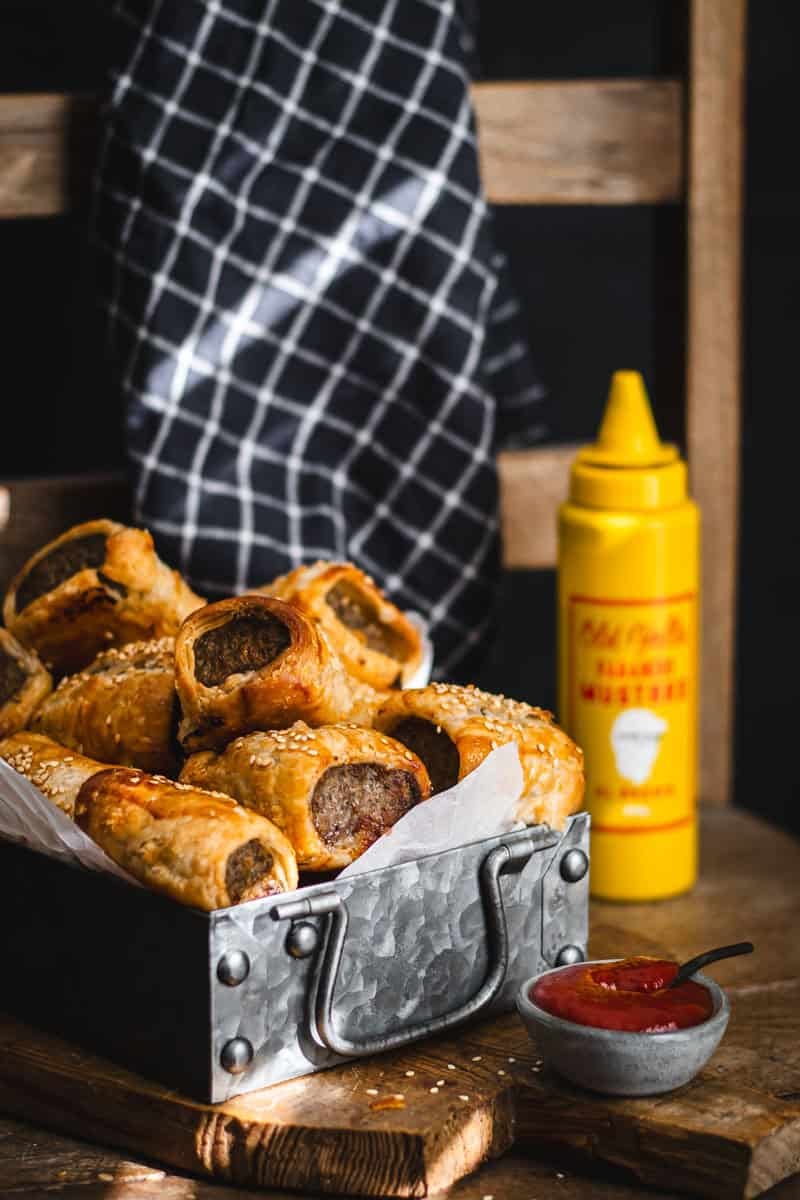 A tray of sausage rolls with ketchup and mustard.
