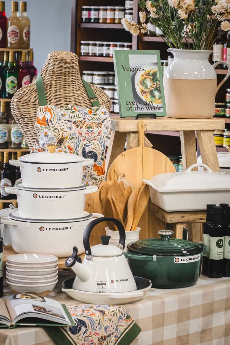 A black Le Creuset and a white Staub cast iron pot sit on a chair with a check tea towel draped over the back.