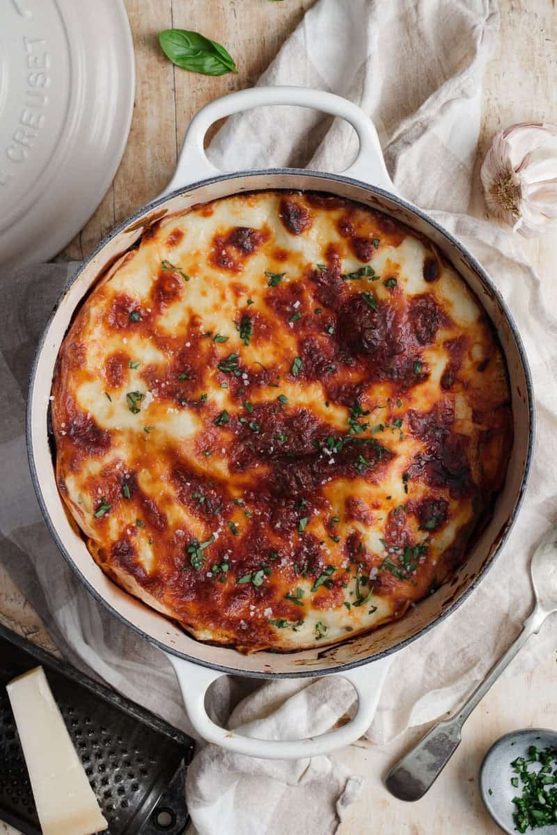 A cream coloured Le Creuset Dutch oven with a baked lasagna in it.