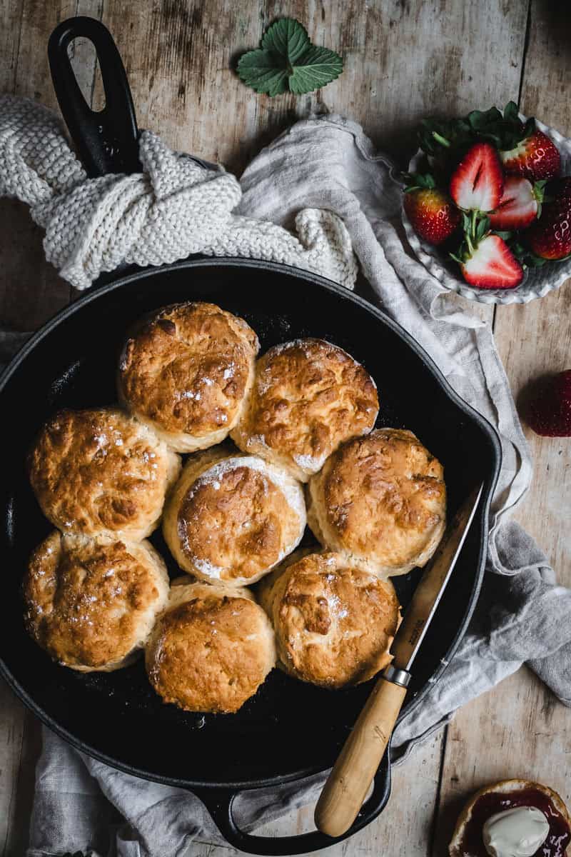 A skillet of scones with fresh strawberries, jam and cream.