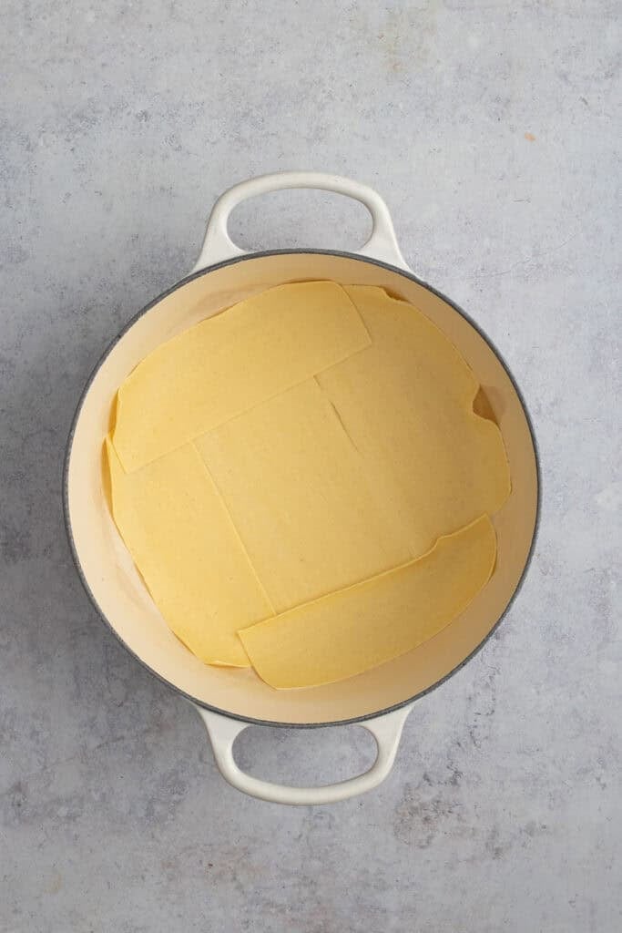 A dutch oven with the base covered in lasagna noodles.