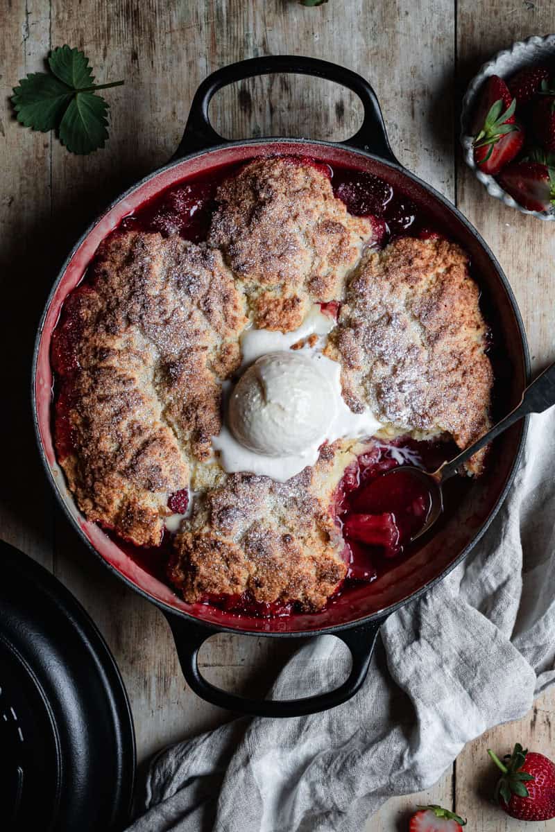 A Dutch oven with a strawberry cobbler baked into it. A scoop has been eaten out of it.