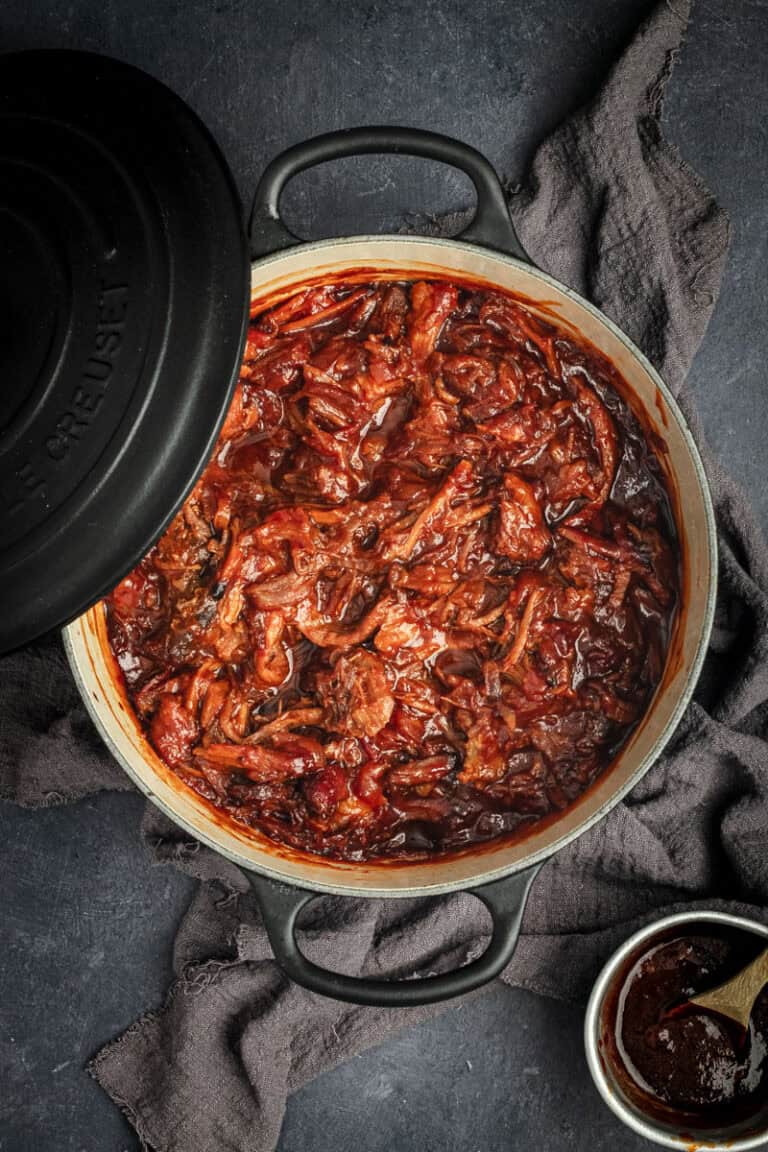 A black Dutch oven of BBQ pulled pork in it.
