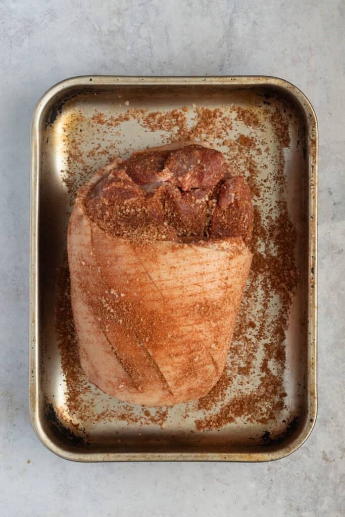 A pork shoulder in a roasting pan marinating in the pork rub.