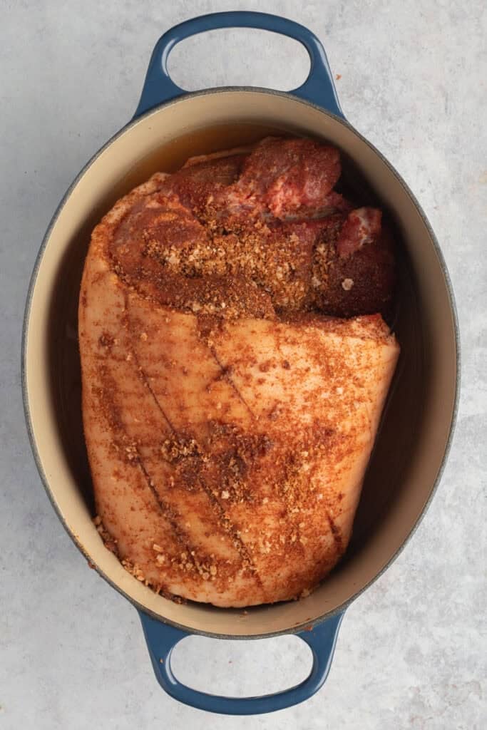An oval Dutch oven with a pork shoulder ready to go into the oven.