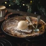a shallow dutch oven by a Christmas tree with a bread and butter pudding baked in it.