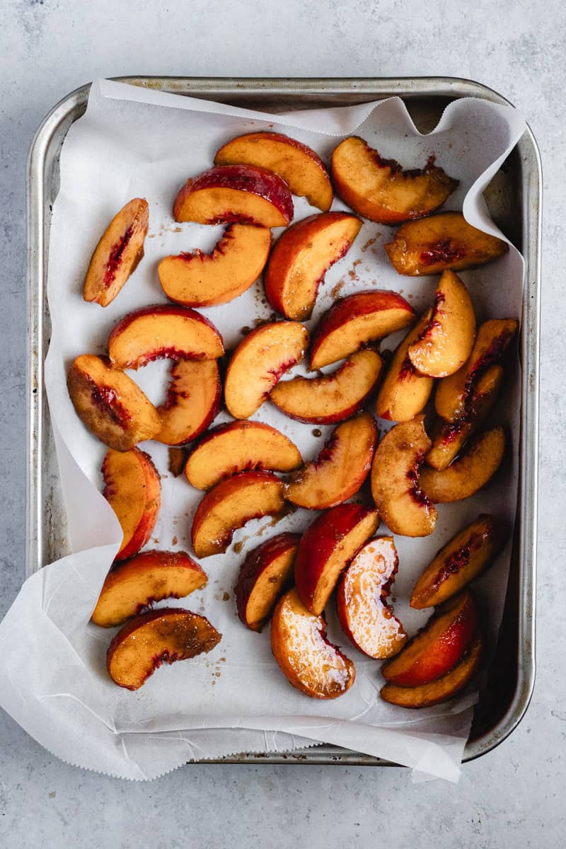Peaches on a baking tray macerating if sugar and spice before they go into the oven.