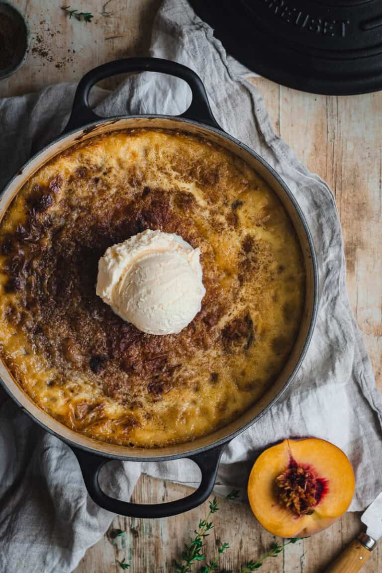 A black cast iron Dutch oven with a peach and custard pudding in it.