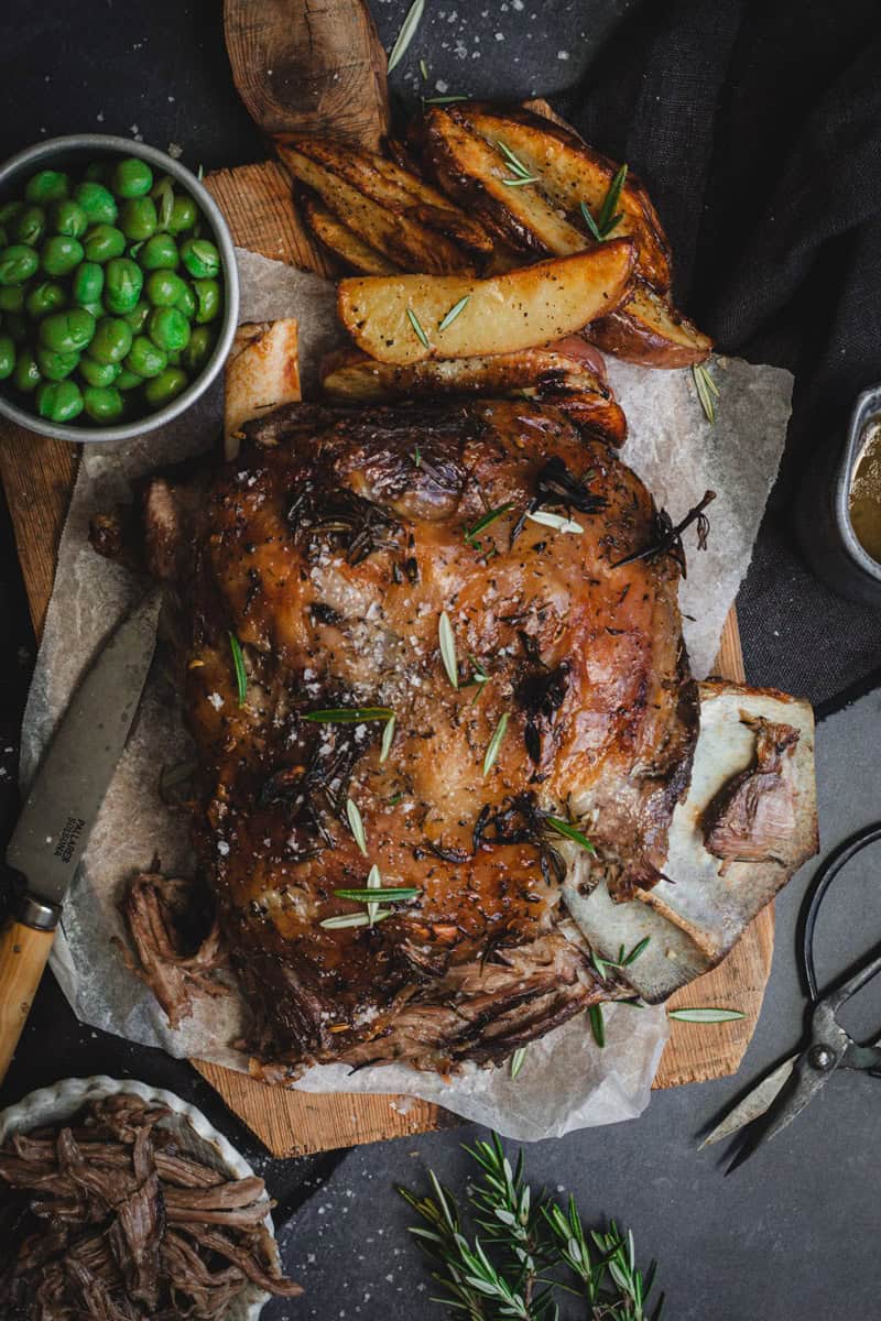 A Dutch oven lamb shoulder from above with side on a timber board.