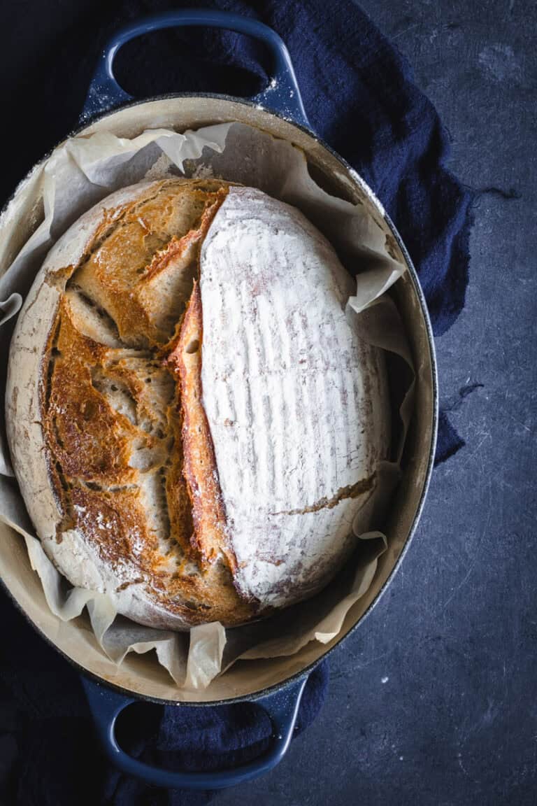 A blue oval Dutch oven with a load of freshly baked sourdough in it.