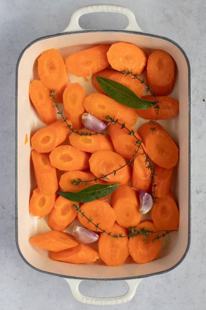 An enamel cast iron roaster with raw carrots ready for the oven.