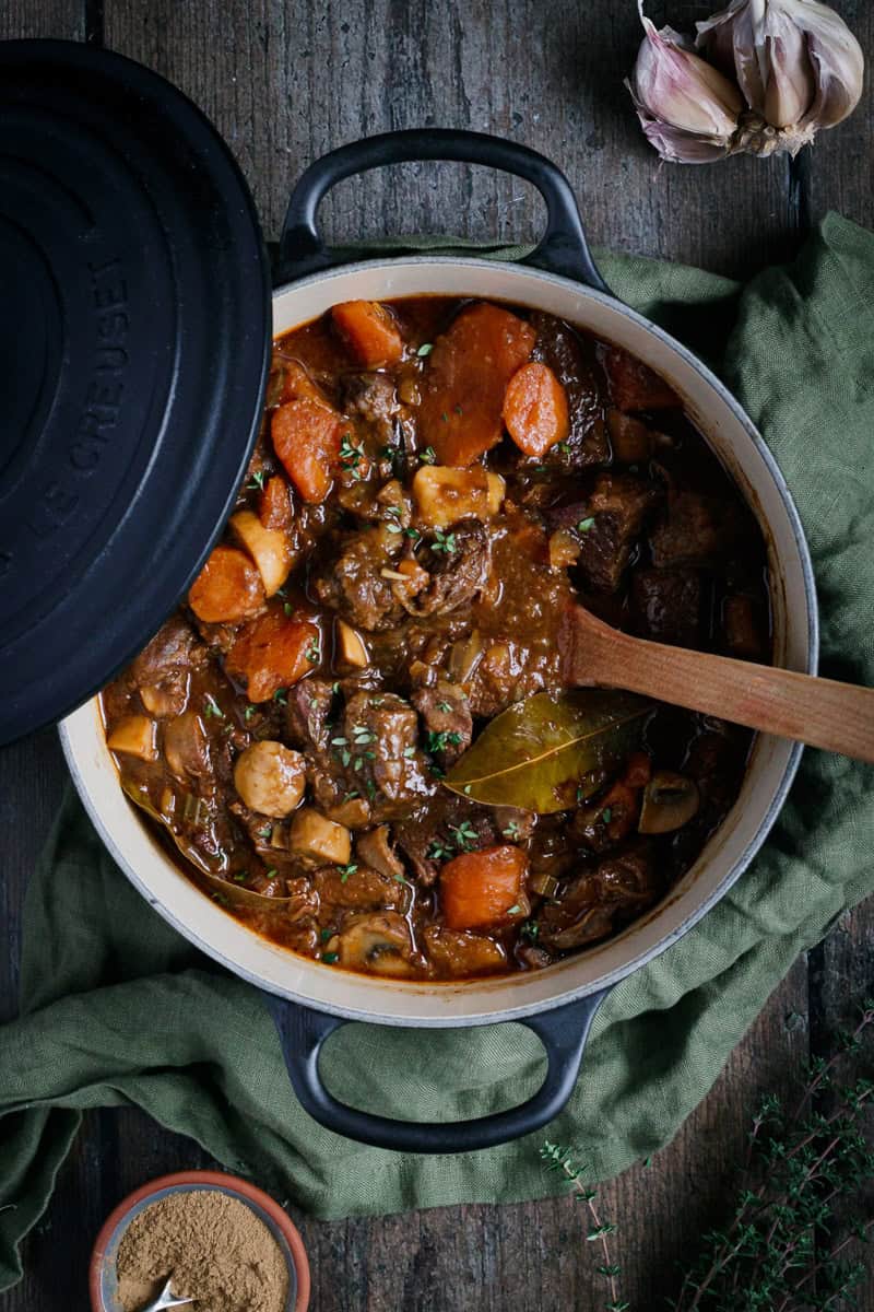 A cast iron pot of beef stew with a wooden spoon in it.